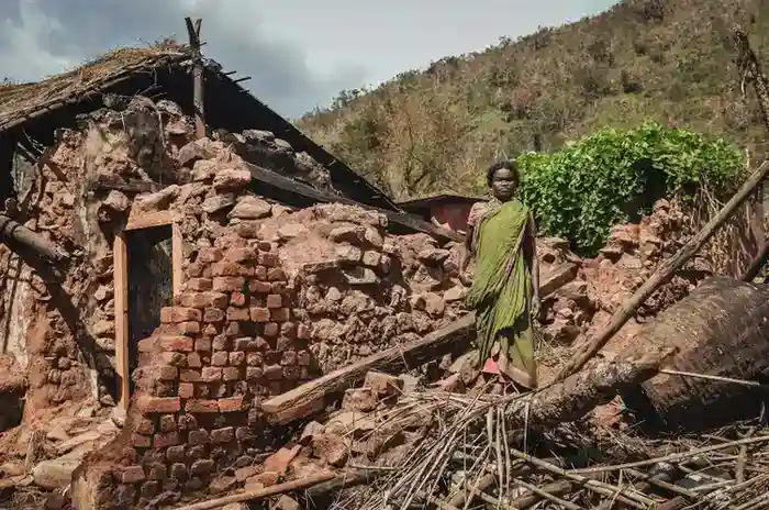 Woman standing amid ruins of her home with brick walls collapsed and roof completely destroyed after devastating cyclone